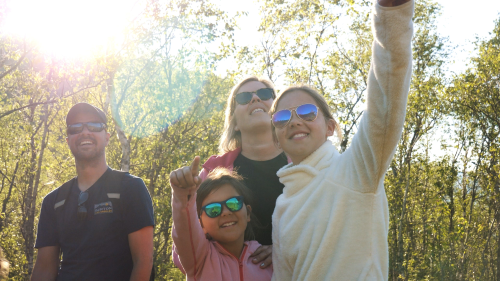 Familie på tur. Far, mor og to jenter ved Stetinden. Sol i bakgrunnen.